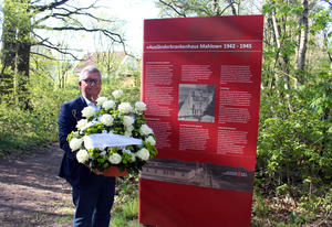 Bürgermeister Michael Schwuchow legt ein Blumengesteck am Ausländerkrankenhaus nieder